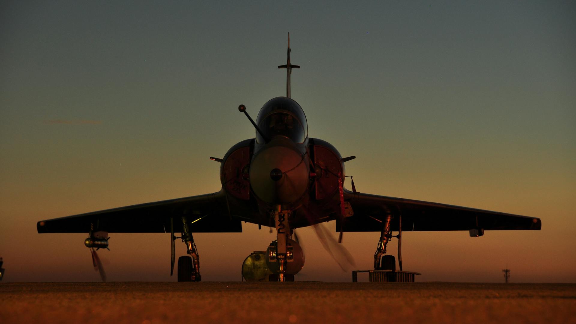 Front view of a Mirage jet fighter on the ground during sunset, featuring a dramatic sky.